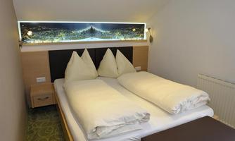 A cozy bedroom with a large double bed and two original pillows shaped like mountains. The walls are painted in neutral colors, and there is atmospheric lighting above the bed.