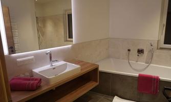 A modern bathroom with a bathtub and a sink on a wooden table. Red towels are placed next to the sink.