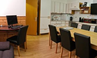 A modern living room with an open kitchen. The room features a dining area with a large table and black chairs.