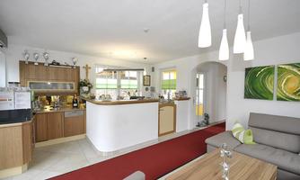 A modern kitchen with wooden cabinets and a cozy seating area. The room is bright and cheerful with a red tiled floor mat.