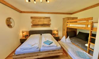 A cozy bedroom with a double bed and a wooden loft bed. The room is bright and furnished in a modern style, with warm wooden details.