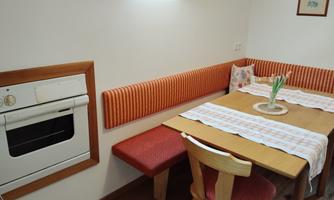 A cozy dining area with a wooden tray and a padded bench. There is an oven and fresh flowers on the table.