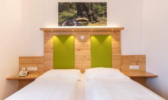 A cozy bedroom with two single beds and a wooden panel wall. Above the beds hangs a picture of a forest scene.