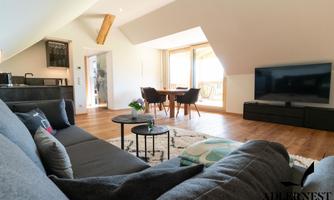 A modern living room with a cozy sofa, a table, and a large television. The large windows offer a view of the surrounding landscape.