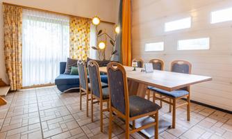 A modern dining room with a wooden table and six chairs. Large windows provide plenty of daylight and a bright atmosphere.