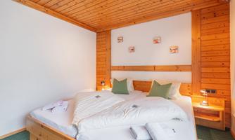 A cozy bedroom with wooden ceilings and a large double bed. The walls are light, and there are midnight blue light sources that create a pleasant atmosphere.