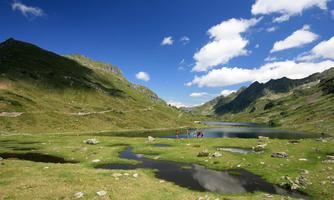 A picturesque landscape with mountains and a clear lake. In the background, some people can be seen enjoying nature.