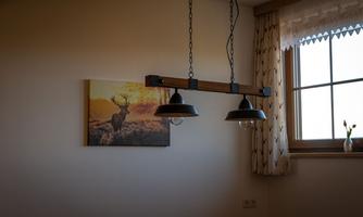 A cozy room with a large window overlooking nature. On the wall hangs a picture of a majestic deer and a stylish lamp hangs from the ceiling.