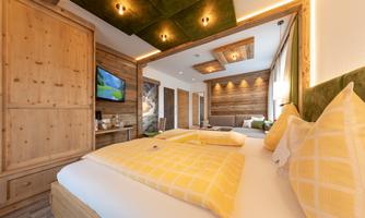 A modern bedroom with wood paneling and a cozy atmosphere. The two beds are decorated with yellow pillows, and a TV is mounted on the wall.
