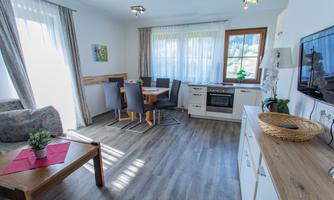 A bright, modern apartment with a kitchenette and dining area. Bright curtains let in plenty of light and create an inviting atmosphere.