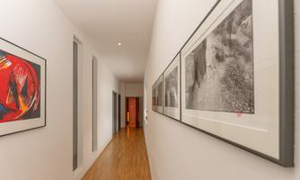 A long corridor with a wooden floor and white walls. Several framed pictures in black and white and color are hung on the wall.