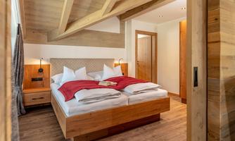 A cozy bedroom with a large double bed and wooden decor. Soft pillows and a red blanket give the room an inviting atmosphere.
