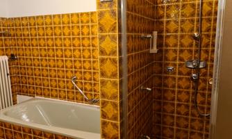 A bathroom with orange tiles and a bathtub. The shower is modern and located next to the bathtub.