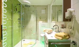 A modern bathroom with a glass shower and green wall tiles. Several handy yellow towels are placed on the sink.