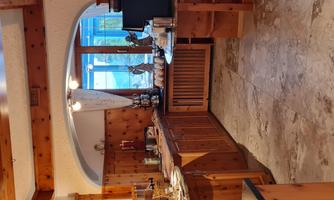 A cozy kitchen with wooden paneling and a large window that lets in a lot of light. Breakfast items and a coffee maker are visible on the countertop.