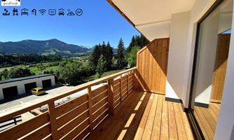 A beautiful balcony with a wooden floor and a view of the surrounding mountains. The surroundings are green and sunny, ideal for relaxing.