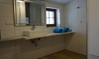 A modern bathroom with a large mirror and a sink. Several blue towels are lying on the shelf.