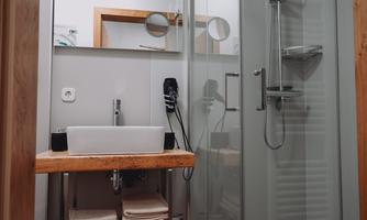 A modern bathroom with a glass shower and a sink on a wooden block. Towels are neatly placed under the sink.