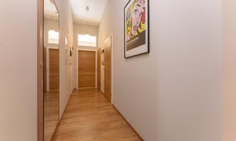 A bright hallway with wooden flooring and several doors. An artistic picture hangs on the wall.