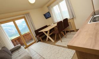 A modern kitchen with a dining table and a cozy seating area. Large windows offer a beautiful view of the Alps.