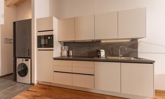 A modern kitchen with bright furniture and an elegant countertop. In the background, a stove, a sink, and a washing machine are visible.