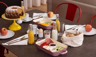 A beautifully set breakfast table with a variety of foods, including fruit, cold cuts, and cheese. Accompanying this are drinks like juice and milk, as well as a chocolate cake.