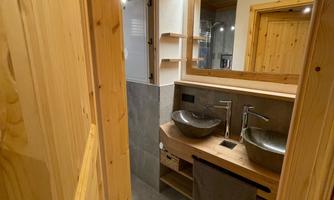 A modern bathroom with wood paneling and two sinks. The decor is simple and stylish, with enough storage space.