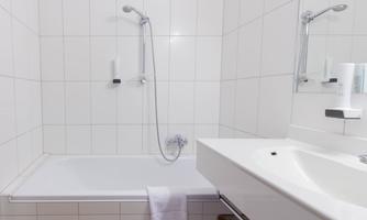 A modern bathroom with a bathtub and a sink. The walls are tiled with white tiles and there is a mirror on the wall.