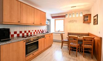 A modern kitchen with wooden furniture and a dining area. The walls are decorated with red and white tiles.