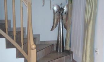A staircase with a decorative angel and plants in a cozy room. The walls are bright and the curtains are in soft colors.