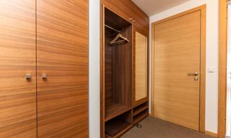 A modern hallway with wooden cabinets and an open wardrobe. The walls and doors are in a light wood tone.