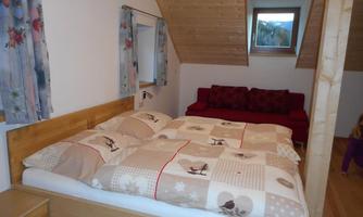 A cozy room with a double bed and a red couch. The walls are bright, and the wooden ceiling gives a warm atmosphere.