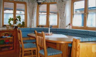 A cozy dining area with a round table and wooden chairs. The windows let in plenty of light and the walls are pleasantly decorated.