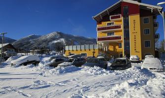 A hotel building with colorful façades stands amidst snow. Cars are partially covered by the snow blanket, and the surrounding mountains are visible in the background.