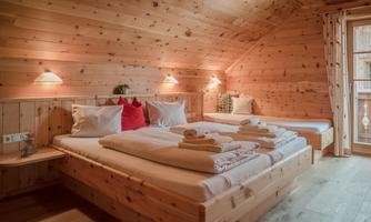 A cozy bedroom with wooden paneling and two beds. The room is brightly lit and offers a beautiful view of nature.