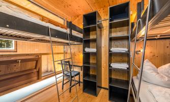 A cozy sleeping area with bunk beds and wooden paneling. There is a chair and shelves with fresh towels.