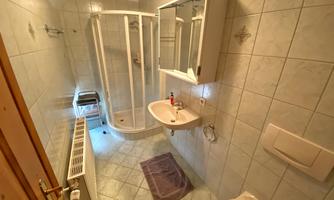 A modern bathroom with a shower, a sink, and a mirror. The walls are decorated with tiles in light colors.