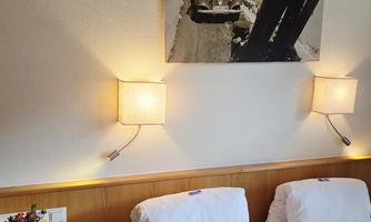A cozy bedroom with two beds and modern wall decoration. The soft lighting creates a relaxed atmosphere.