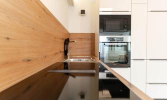 Modern kitchen with an elegant wood paneling and black work surfaces. In the background, a microwave and an oven are visible.