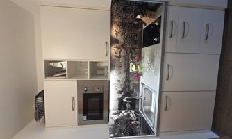 A modern kitchen with a sink, a microwave oven, and elegant cabinets. The background features a decorative landscape and fresh flowers on the countertop.