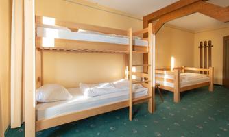 A simple room with two wooden bunk beds. The walls are painted yellow and the floor has a green carpet.