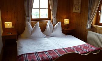 A cozy bedroom with a large double bed and rustic wood paneling. Two nightstands with warm lamps create an inviting atmosphere.