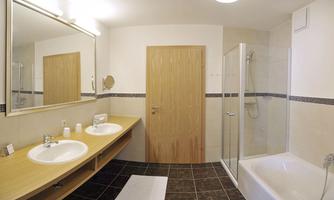 A modern bathroom with two sinks and a large mirror. There is a shower and a bathtub, as well as bright tiles and a wood look.