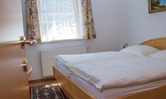 A cozy bedroom with a double bed and a window that lets in daylight. A picture of a landscape hangs on the wall.