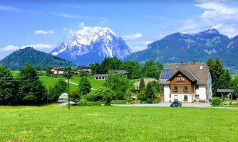 A picturesque landscape with green meadows and mountains in the background. In the foreground, there is a beautiful house on a quiet street.