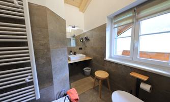 A modern bathroom with elegant tiles and a large window. There is a shower, a sink, and wooden details that create a cozy atmosphere.
