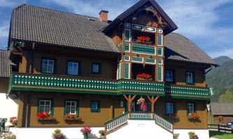 A traditional wooden house in alpine style with colorful flower boxes. The sky is clear and the surroundings are green.