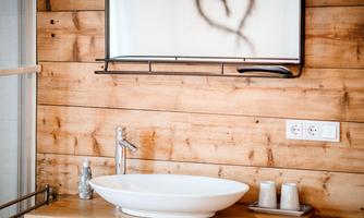 A modern bathroom with a white sink and a large mirror. The walls are made of wood, creating a warm atmosphere.
