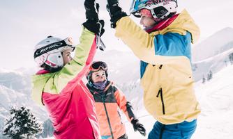 Three skiers are celebrating on the slope in the snow. They are wearing colorful ski outfits and seem to be having a lot of fun.