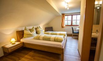 A cozy bedroom with two single beds and hardwood flooring. Large windows provide plenty of daylight.